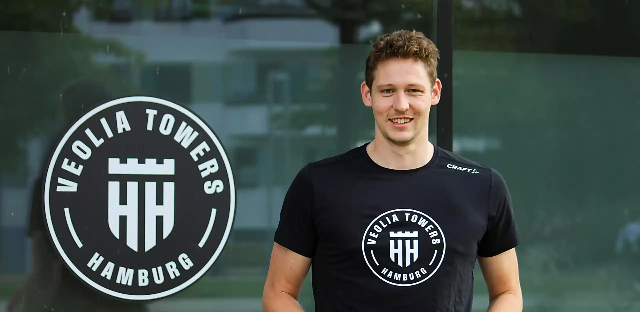 Patrick Heckmann mit Basketball in der Hand vor Veolia Towers Logo an der Inselpark Arena